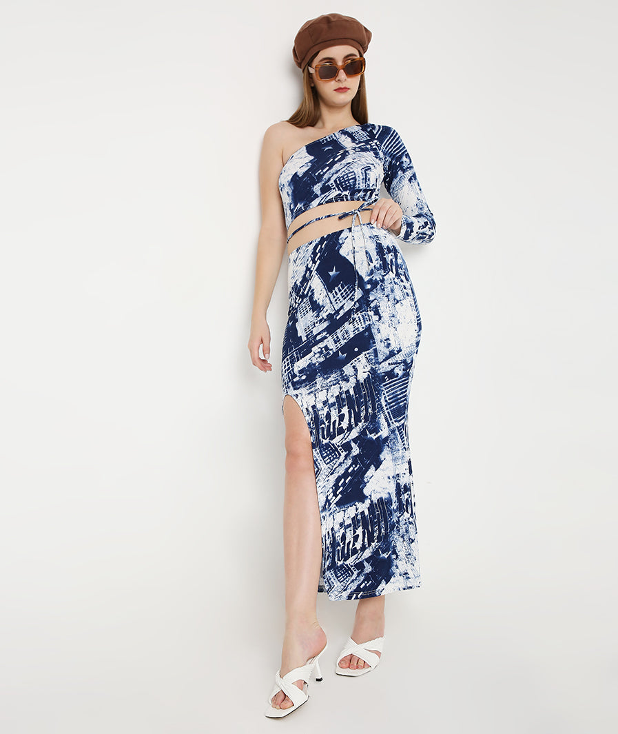 Full-length blue tie-dye co-ord set. Model wearing one-shoulder top and front-cut skirt. Matching print resort outfit. Designer two-piece look. Chic vacation fashion. Modern minimalist matching set. Versatile fashion co-ord. Polished wardrobe staple. Sleek silhouette separation. Casual luxury wear. High-end lifestyle fashion. Premium women apparel. Detailed front-cut skirt. Fitted blue print set.
