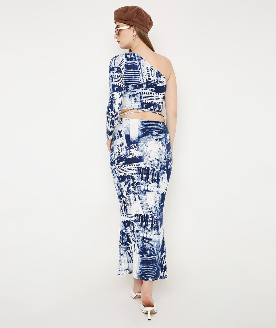Full-length blue tie-dye co-ord set. Model wearing one-shoulder top and front-cut skirt. Matching print resort outfit. Designer two-piece look. Chic vacation fashion. Modern minimalist matching set. Versatile fashion co-ord. Polished wardrobe staple. Sleek silhouette separation. Casual luxury wear. High-end lifestyle fashion. Premium women apparel. Detailed front-cut skirt. Fitted blue print set. Contemporary resort style.