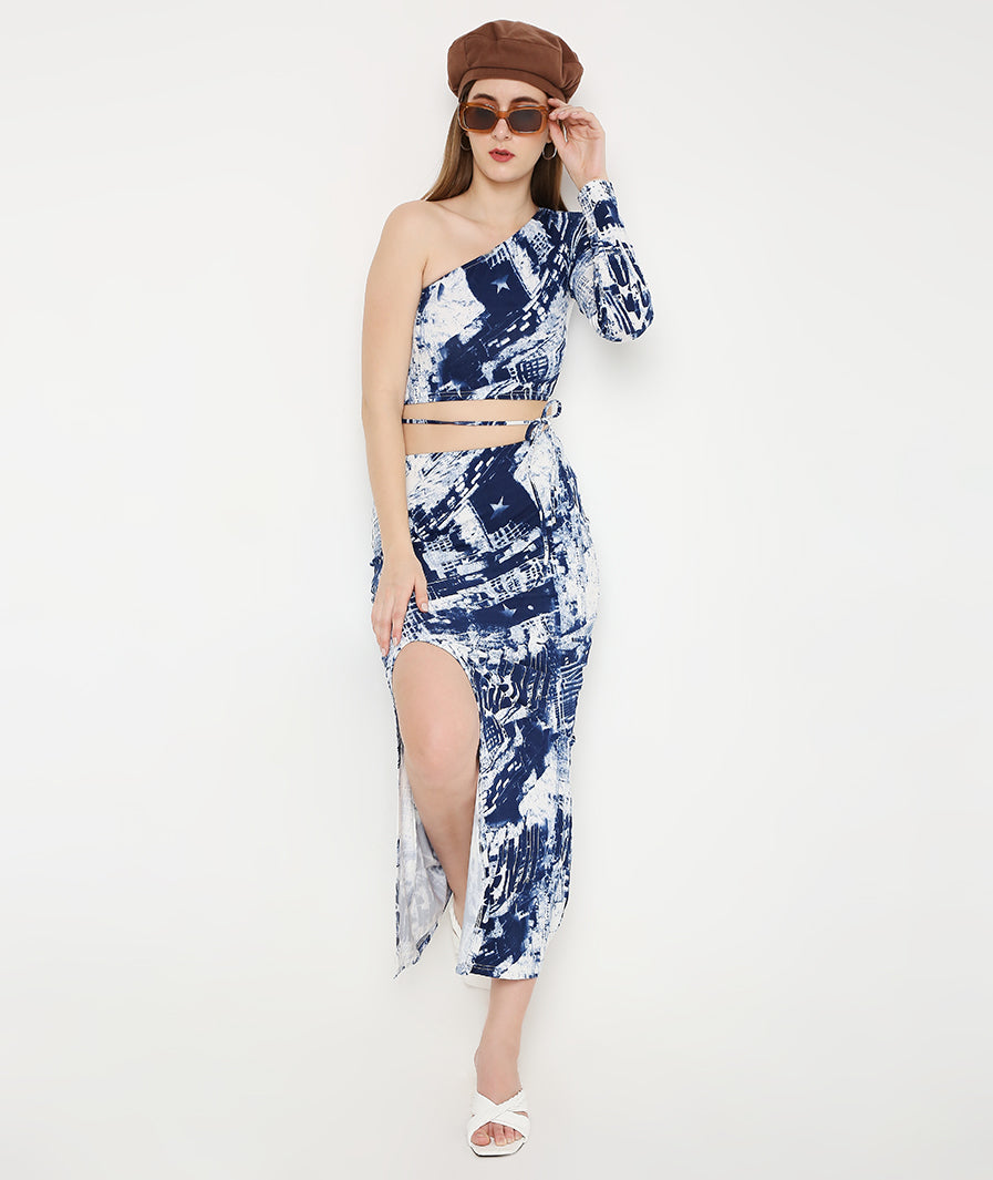 Blue tie-dye front cut skirt view. Detailed slit angle. Asymmetric top close up. Patterned fabric texture. Designer stitching details. Off-shoulder neckline view. Premium apparel fabric finish. High-end clothing craftsmanship. Contemporary fashion zoom style. Elegant silhouette look. Luxury brand clothing detail. Stylish print accent view. Modern apparel design. Clean pattern finish. Sophisticated fabric quality.